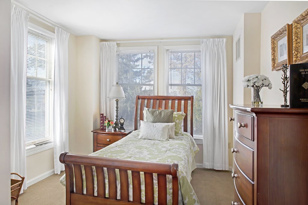 A cozy bedroom with a single wooden bed, dresser, and window view.
