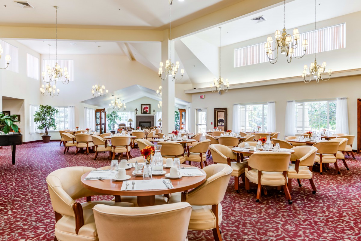 A spacious and elegantly decorated dining area with multiple tables and chairs, featuring chandeliers and a warm ambiance.