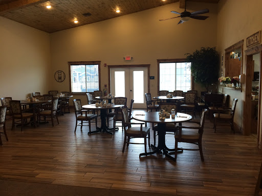 A cozy dining area with wooden floors and ample natural light, featuring tables and chairs arranged for a relaxed setting.