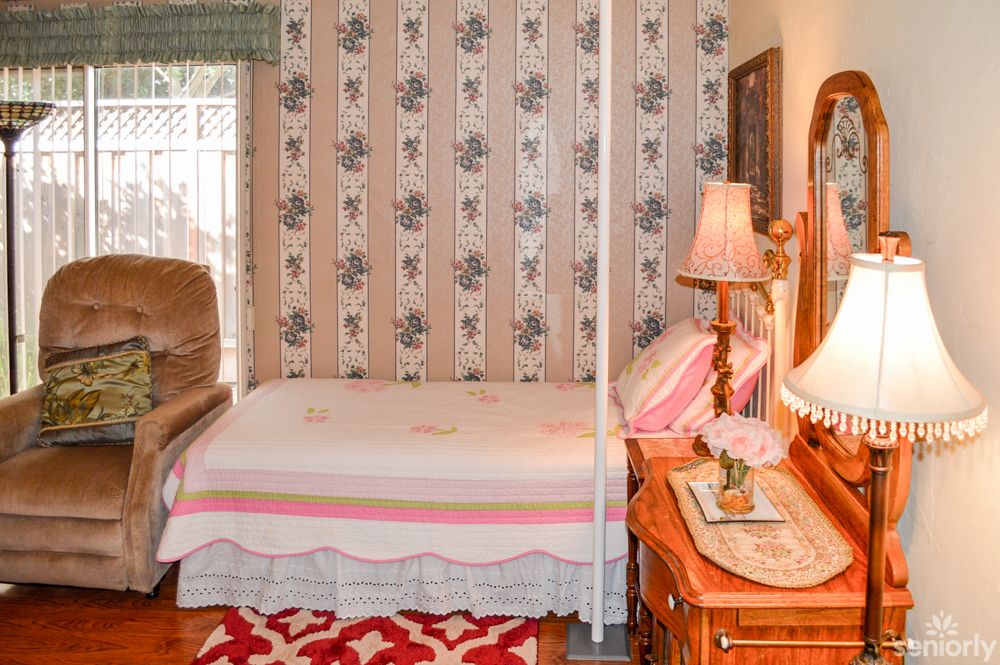 A cozy vintage bedroom with floral wallpaper, a neatly made bed, and classic wooden furniture.