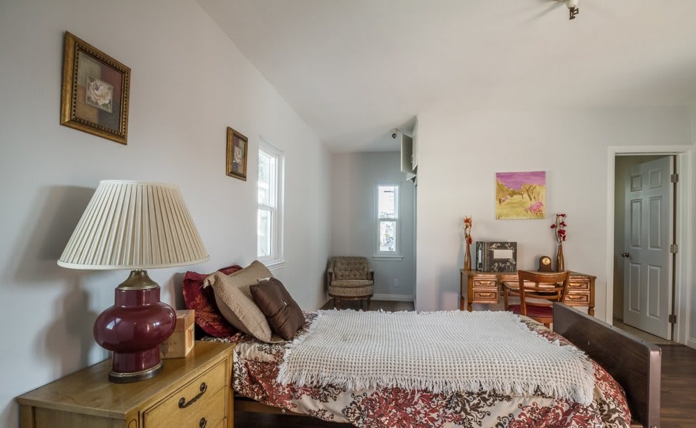 A cozy bedroom with a bed, side table, lamp, and a desk.