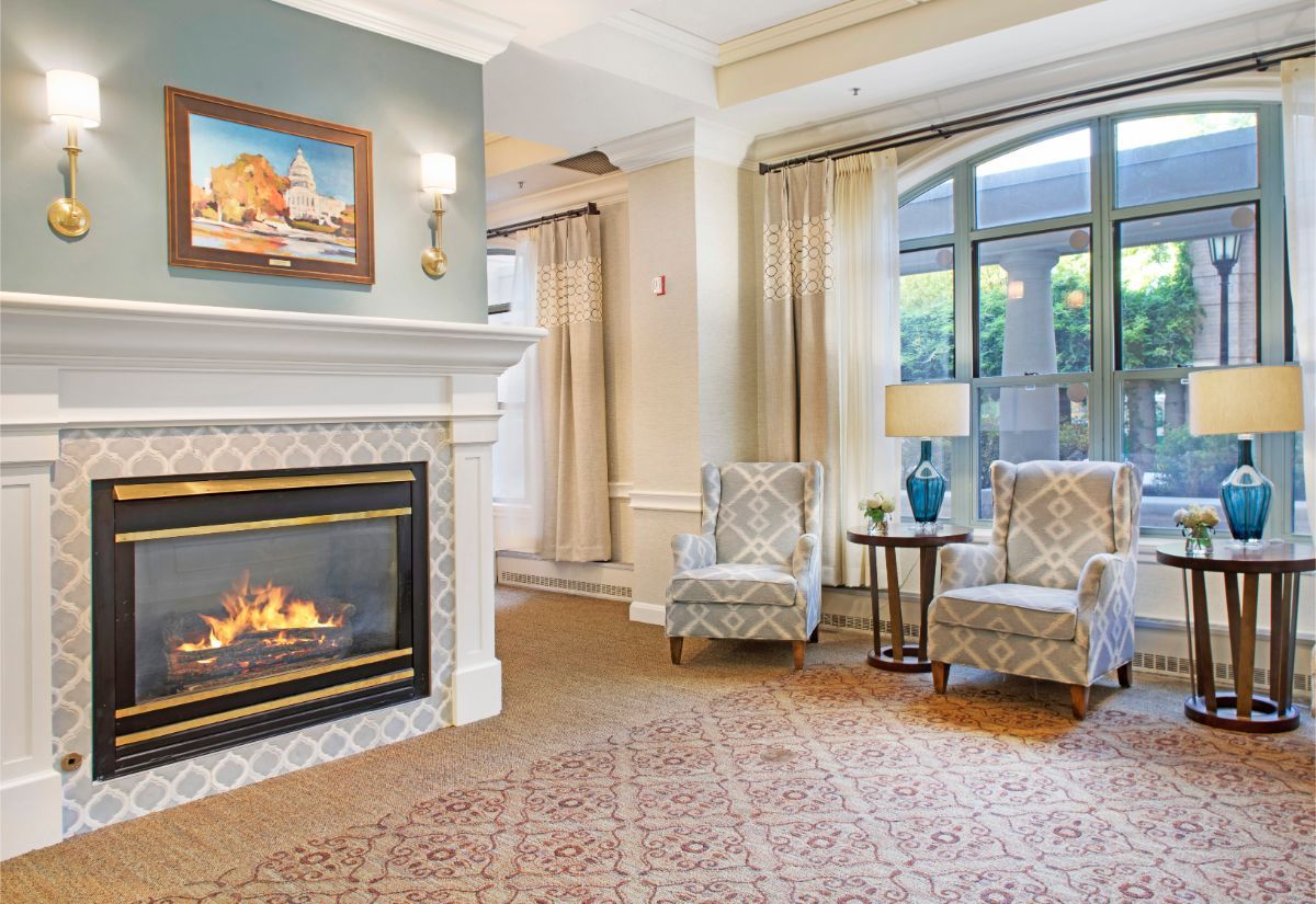 A cozy living room with a fireplace, two chairs, and a large window letting in natural light.