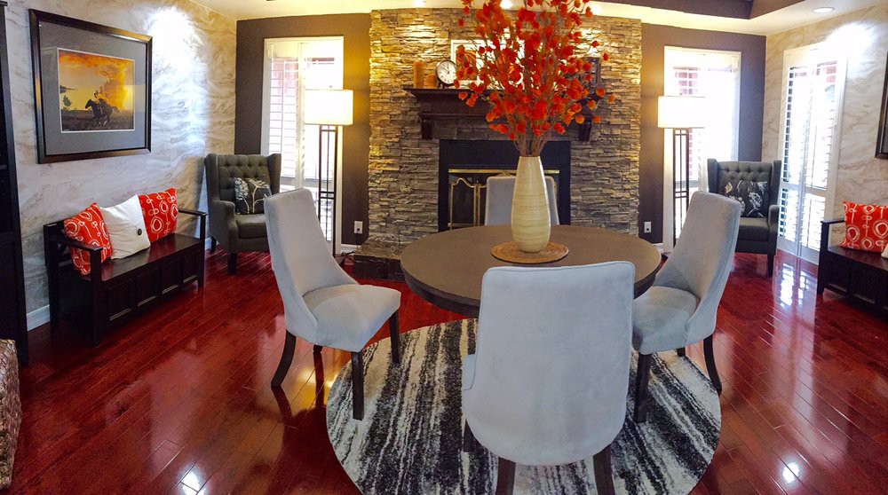 A modern dining room with elegant furnishings, featuring a stone fireplace, round table, and decorative vase centerpiece.