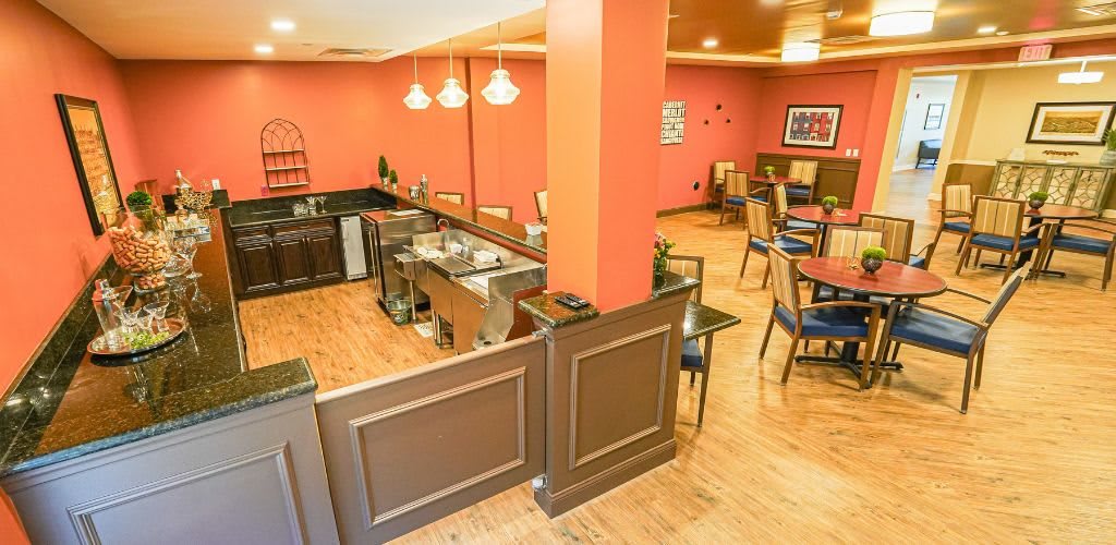 A cozy restaurant interior featuring a bar counter, wooden flooring, and neatly arranged dining tables and chairs.