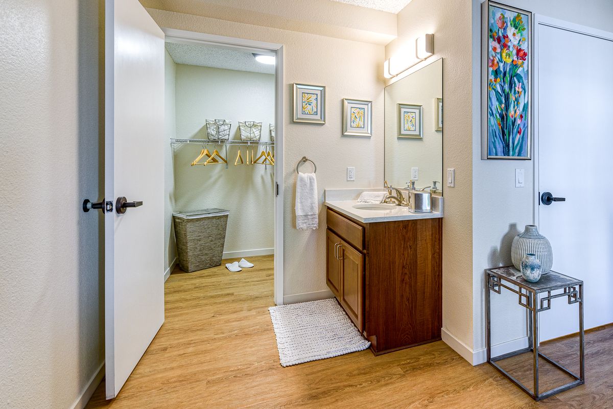 A well-organized bathroom with a wooden vanity, sink, and mirror, leading to a laundry area.
