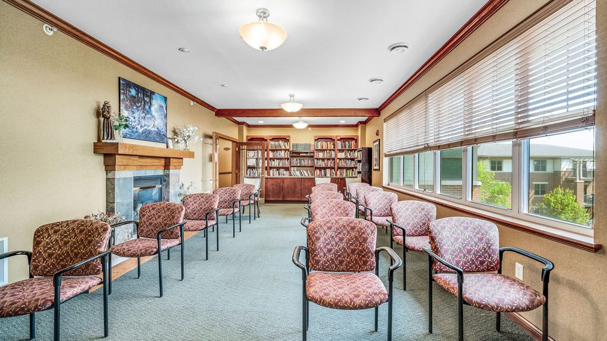 A spacious waiting room with chairs arranged in rows, a television mounted above a fireplace, and bookshelves along the back wall.