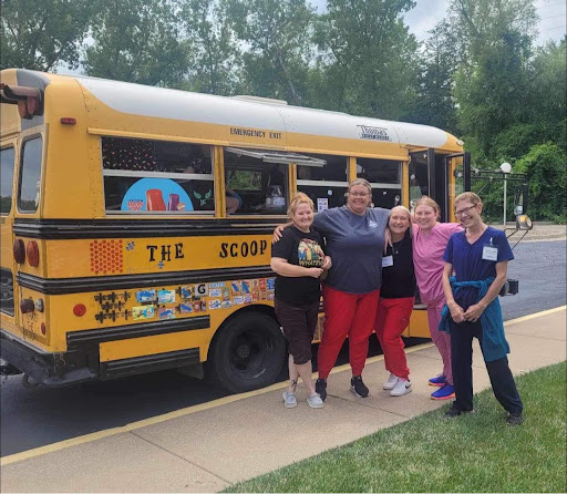 A cheerful group of individuals gathered in front of a colorful school bus, celebrating a community event.