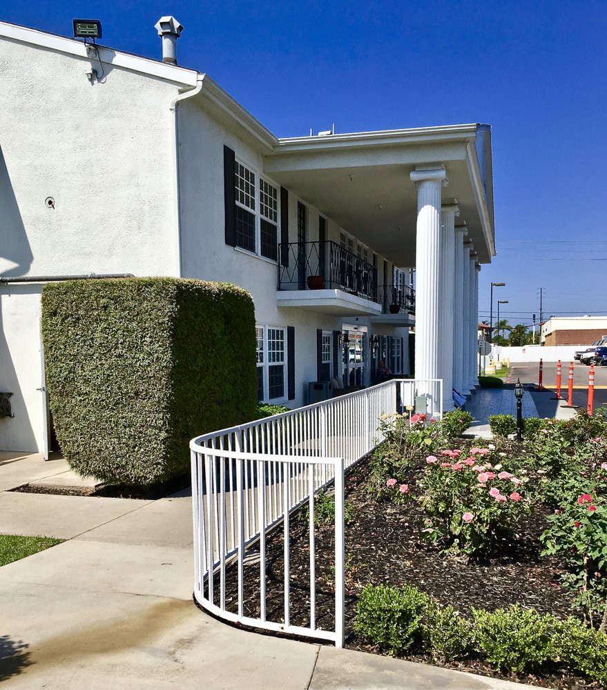 A sunny exterior view of a two-story apartment building with a garden and walkway.