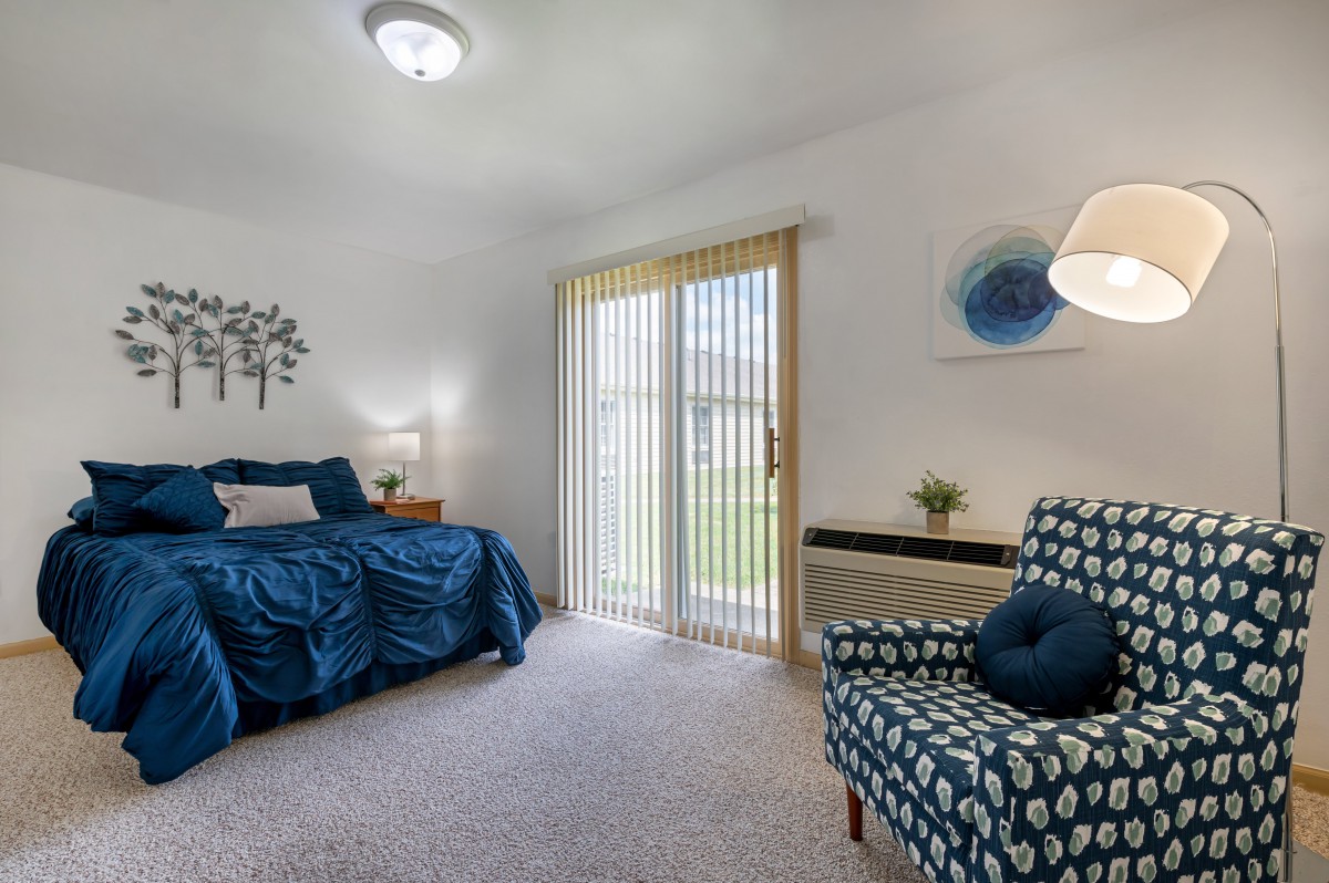 A cozy bedroom with blue accents and natural light coming through vertical blinds.