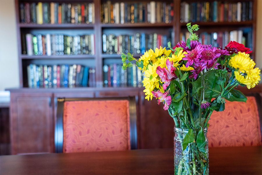 A colorful bouquet of flowers in a vase sits on a table in front of a bookshelf filled with books.