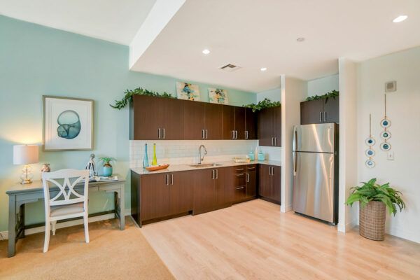 A modern kitchen with dark cabinets, a stainless steel refrigerator, and light wood flooring.