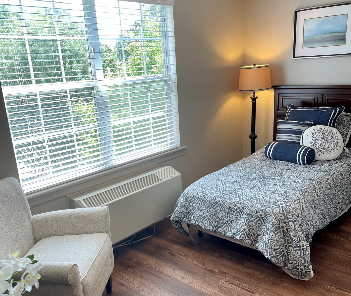 A cozy bedroom with a single bed, a chair by the window, and a floor lamp.