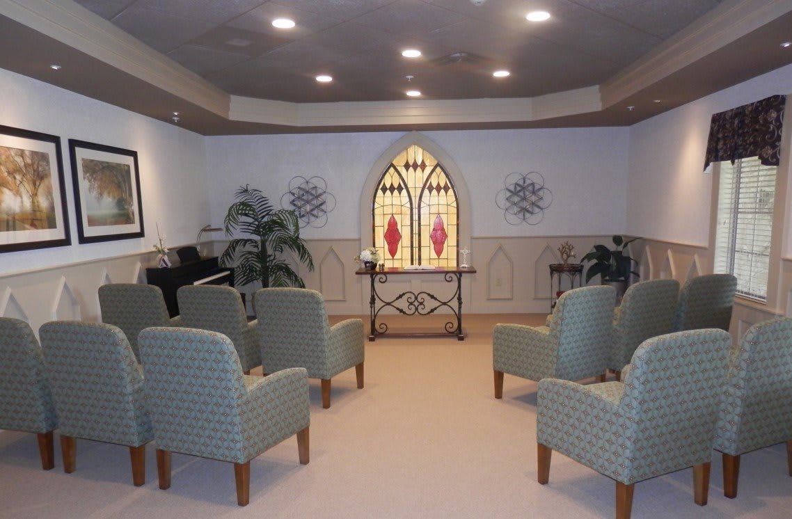 A small chapel with seating, stained glass window, and decorative elements.