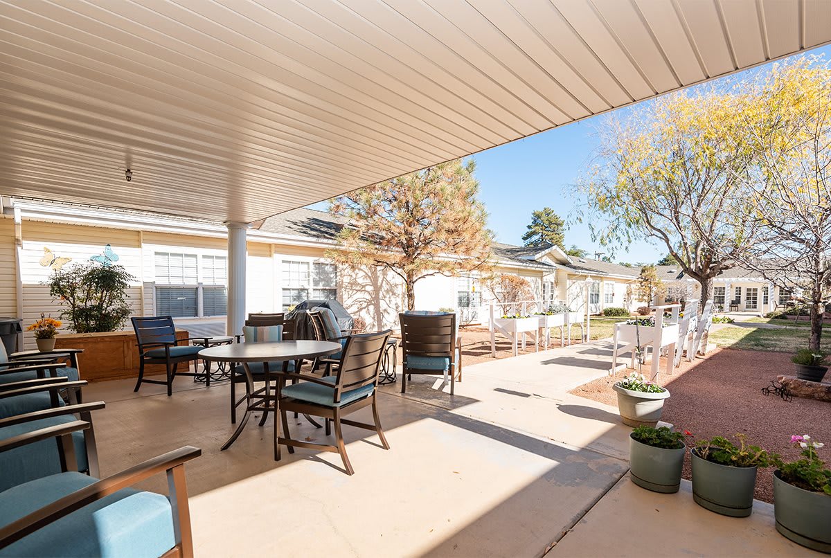 A sunny outdoor patio with several tables and chairs under a covered area.