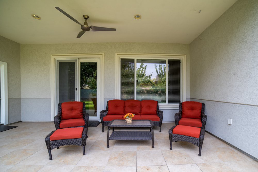 A cozy outdoor patio featuring red cushioned seating and a coffee table under a ceiling fan.