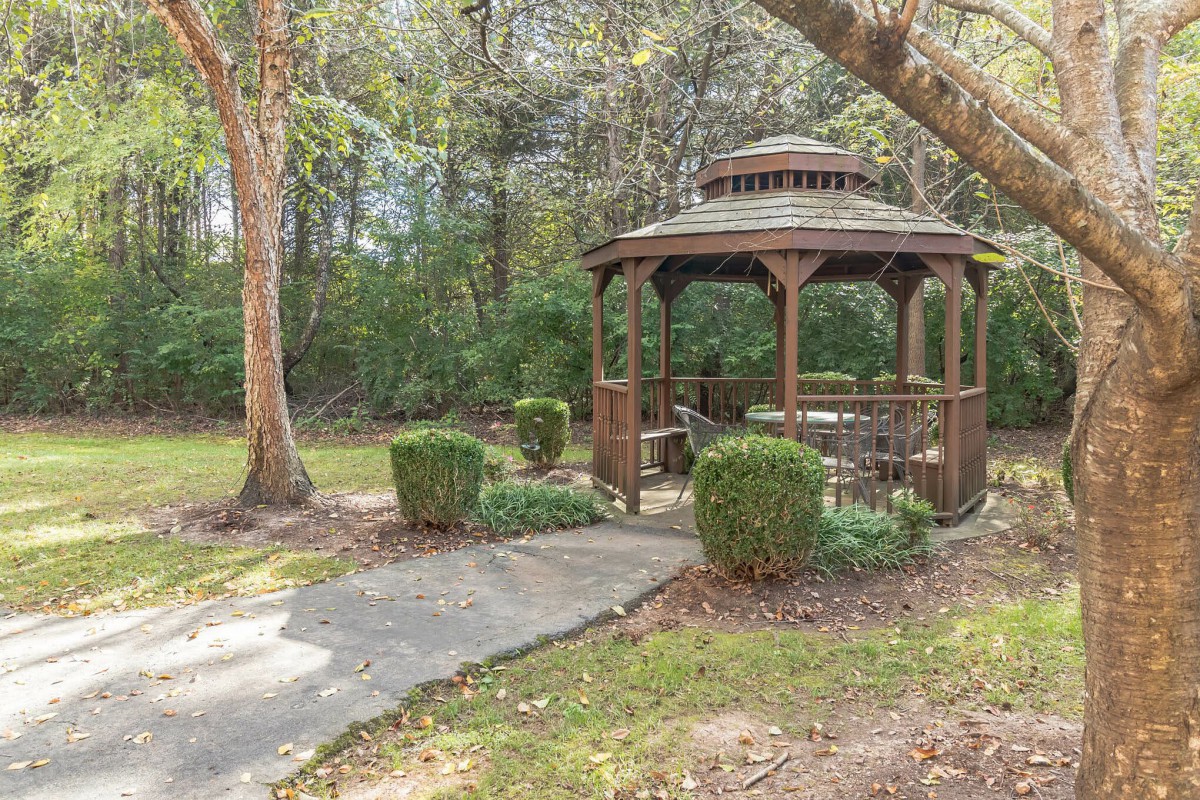 A serene garden with a wooden gazebo surrounded by trees and greenery.