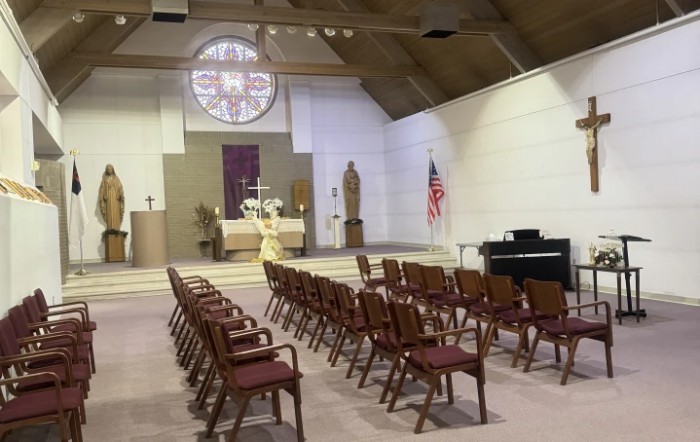 The interior of a church featuring rows of pews, an altar with religious symbols, and a stained glass window in the background.