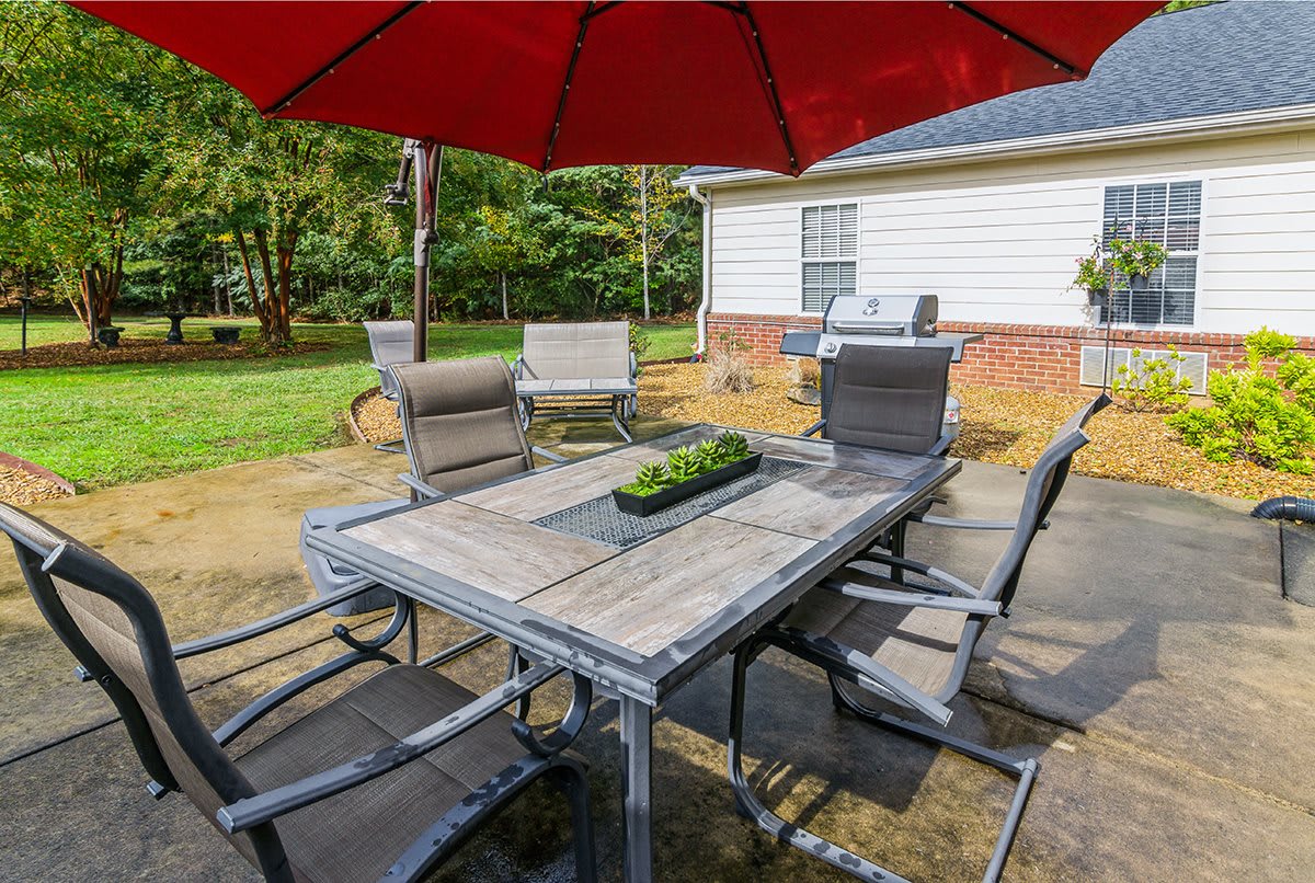A patio setup with a table, chairs, and an umbrella in a backyard setting.