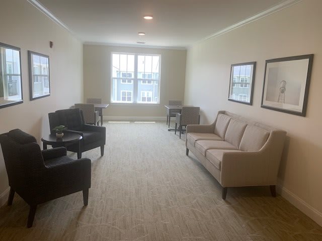 A well-lit living room featuring a sofa, several chairs, tables, and framed artwork on the walls.