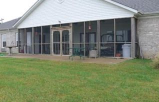 A suburban house with a screened porch and a green lawn in the backyard.