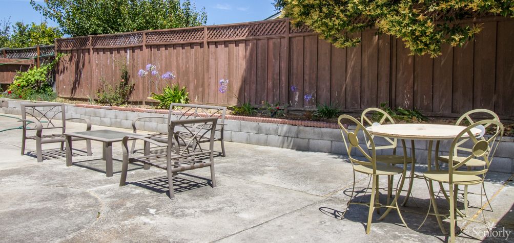 A sunny patio area with outdoor chairs and a table near a wooden fence.