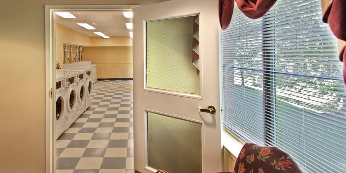 A laundromat interior with a checkered floor and an open door leading to a room with ceiling lights.