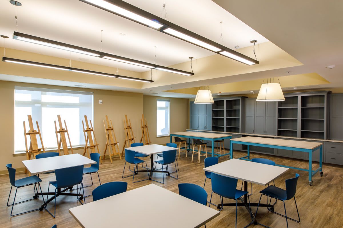 A well-lit art classroom featuring easels, tables, and chairs, creating an inviting space for creativity.