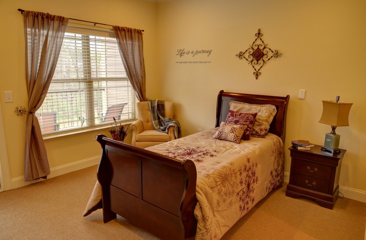 A cozy bedroom with a single bed, decorative pillows, and a comfortable chair by the window.