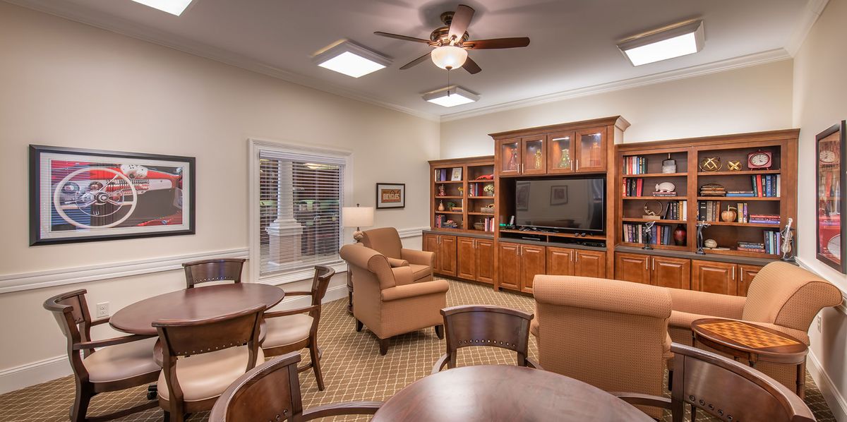 A cozy living room with comfortable armchairs, a large television, and wooden bookshelves.