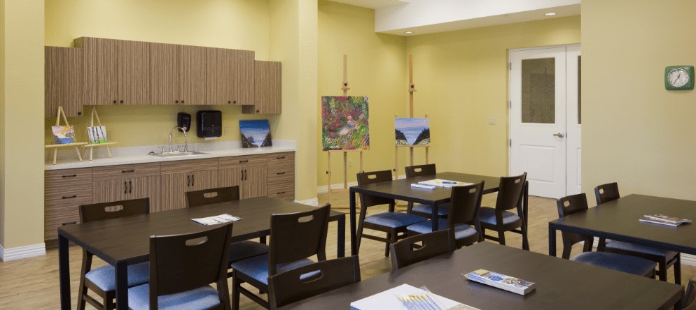 An art room with tables and chairs, featuring paintings displayed on easels.