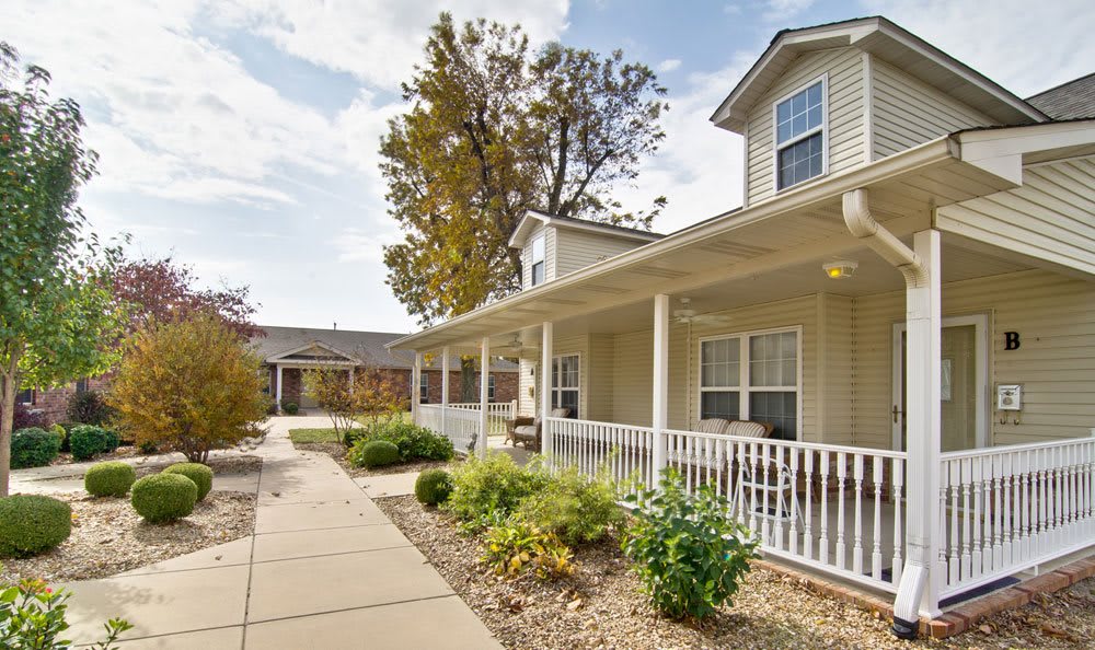 A charming house with a porch, surrounded by a garden and trees under a clear sky.