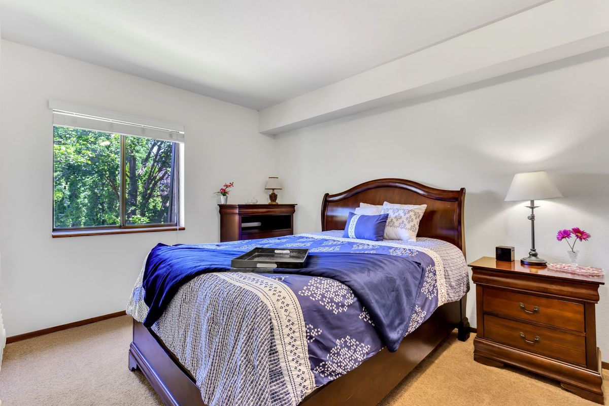 A cozy bedroom with a wooden bed and elegant bedding, featuring a window with a view of trees.