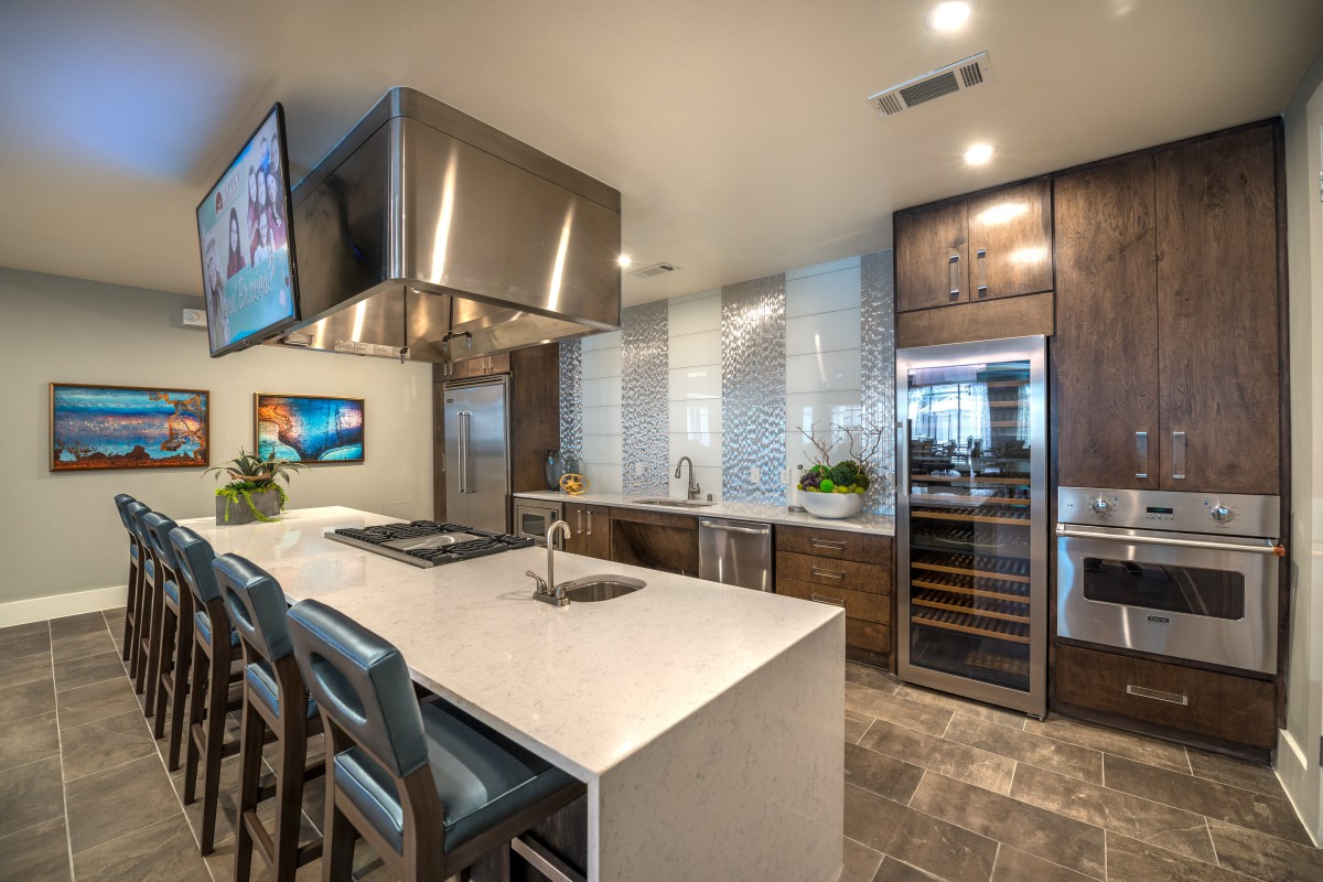 A sleek and modern kitchen featuring a spacious island with seating, stainless steel appliances, a wine cooler, and elegant decor.