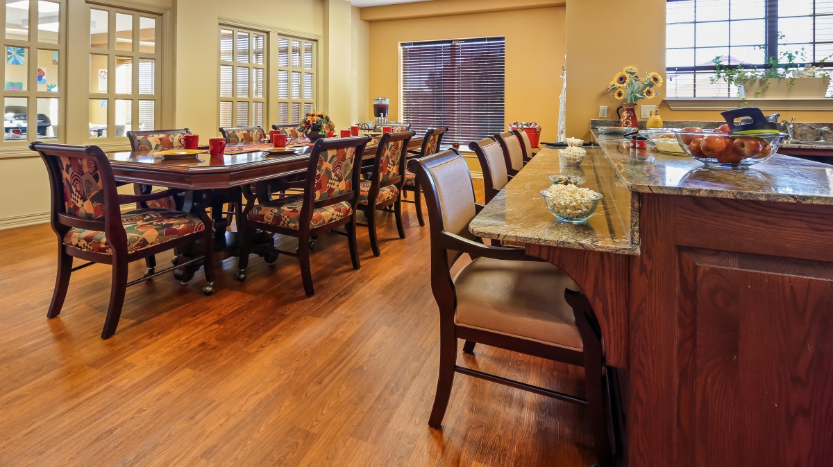 A spacious dining room with a long table, surrounded by chairs and set on a wooden floor.