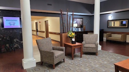 A cozy waiting area featuring two plush chairs, a wooden table with a flower arrangement, and soft lighting.