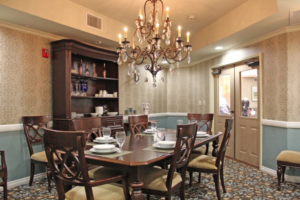A traditional dining room featuring a wooden table set with place settings, surrounded by chairs and illuminated by an elegant chandelier.