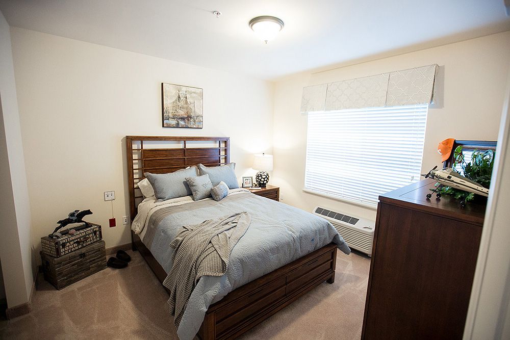 A cozy and well-decorated bedroom with a neatly made bed, wooden furniture, and ample natural light.