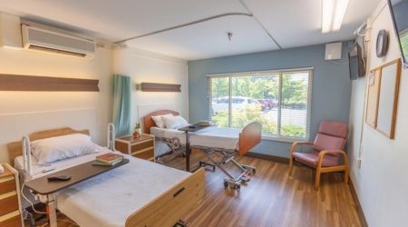 A well-lit hospital room with two beds, a large window, and modern furnishings.