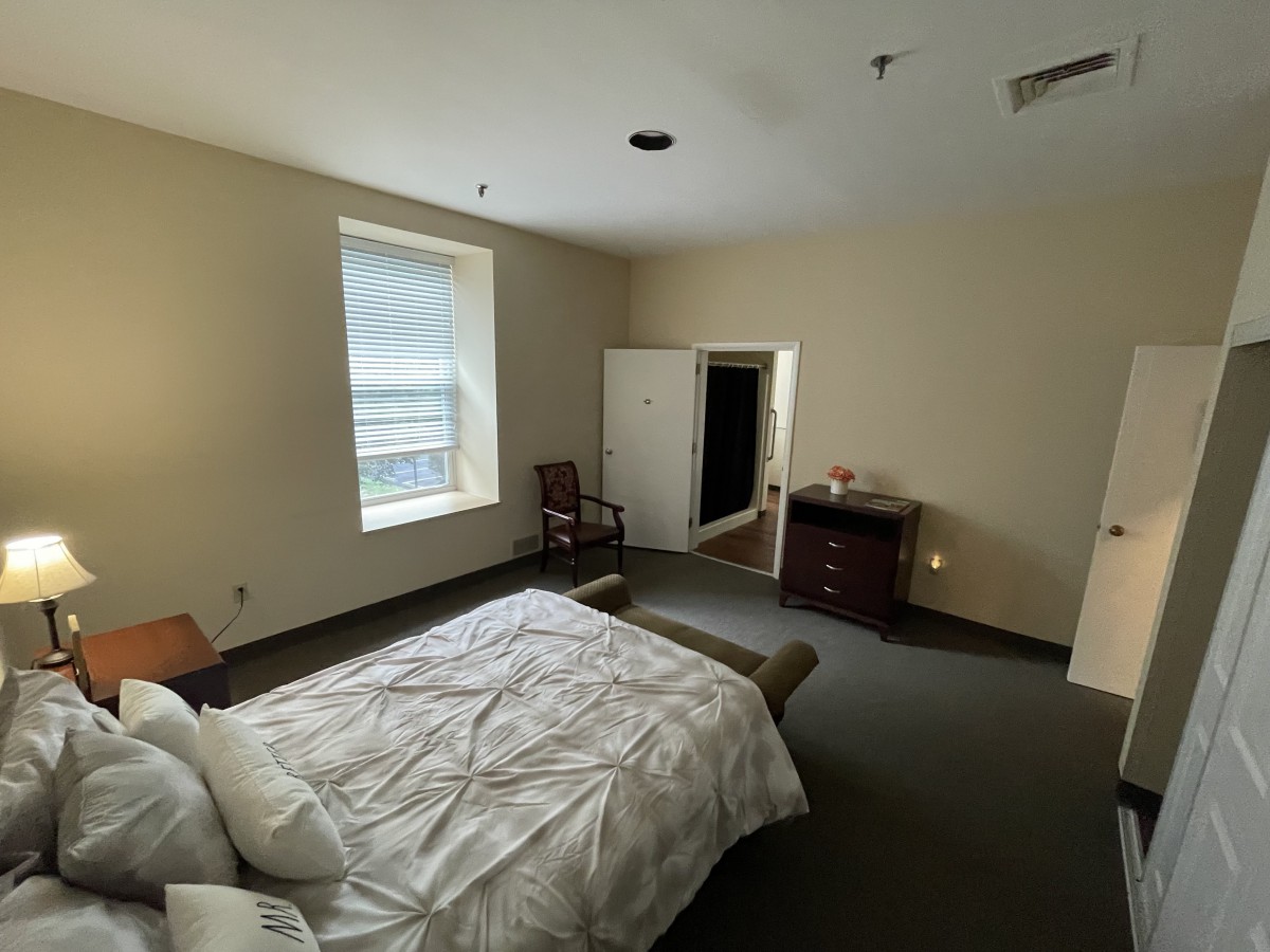 A tidy bedroom featuring a bed, chair, window, and dresser.