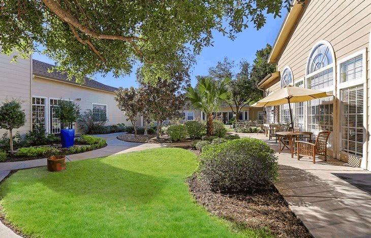 A well-maintained garden with lush greenery and a patio area under a sunny sky.