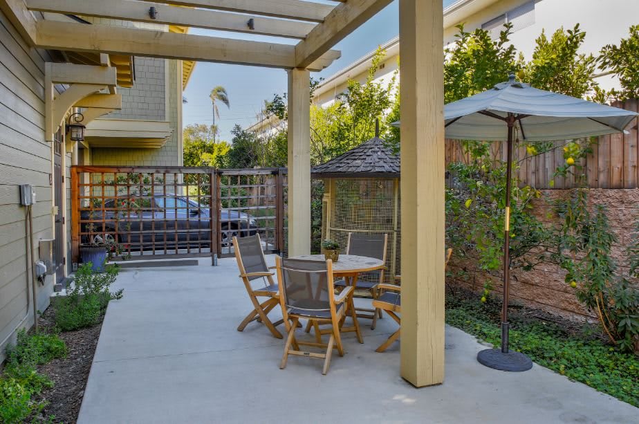 A cozy outdoor patio setup with a table, chairs, and an umbrella under a pergola.