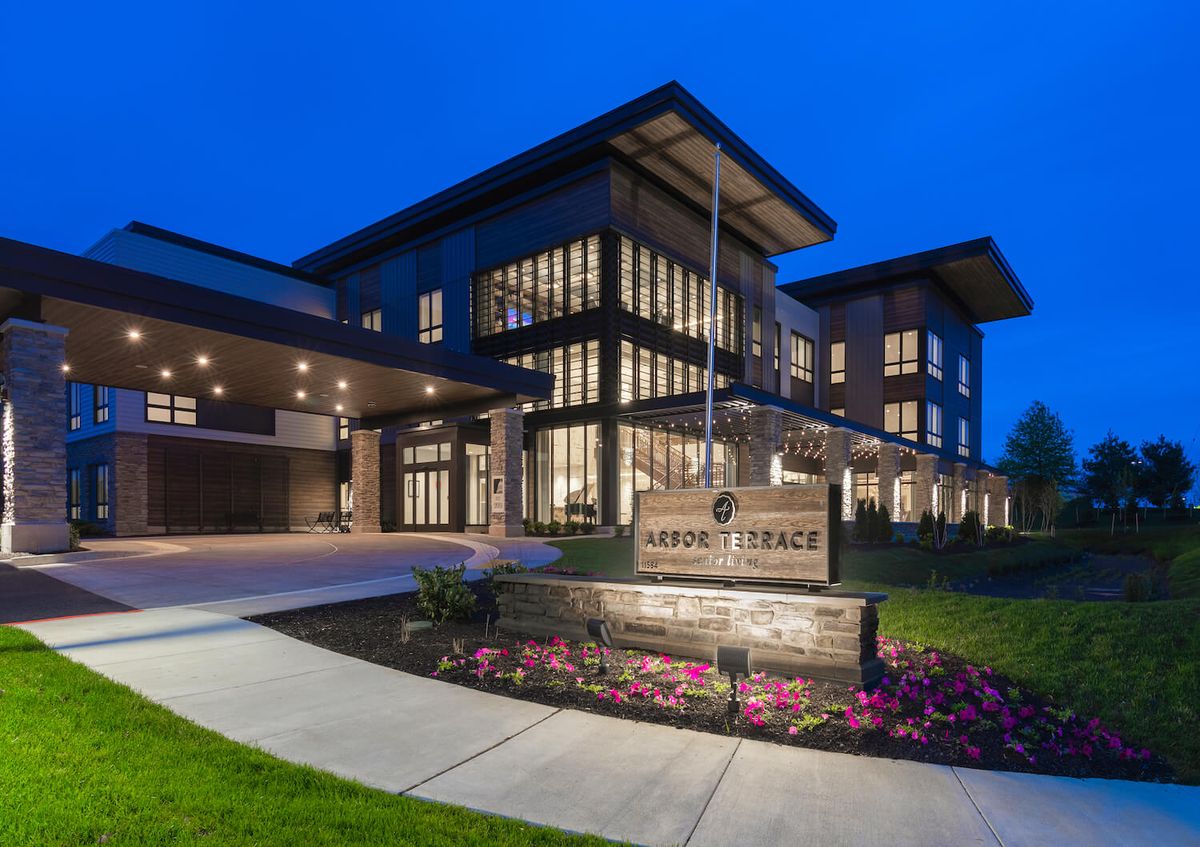 A modern building illuminated at night with a well-lit entrance and landscaped surroundings.