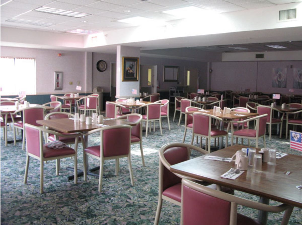 An empty dining hall with arranged tables and chairs, bathed in natural light.