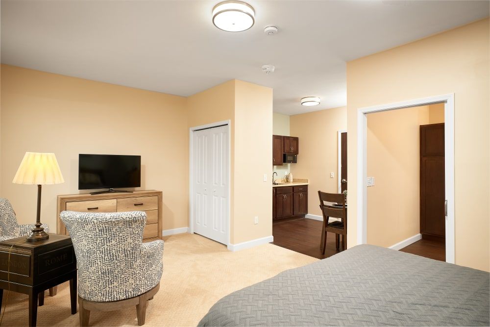 A cozy bedroom with a TV, dresser, and chair, adjacent to a kitchenette area.