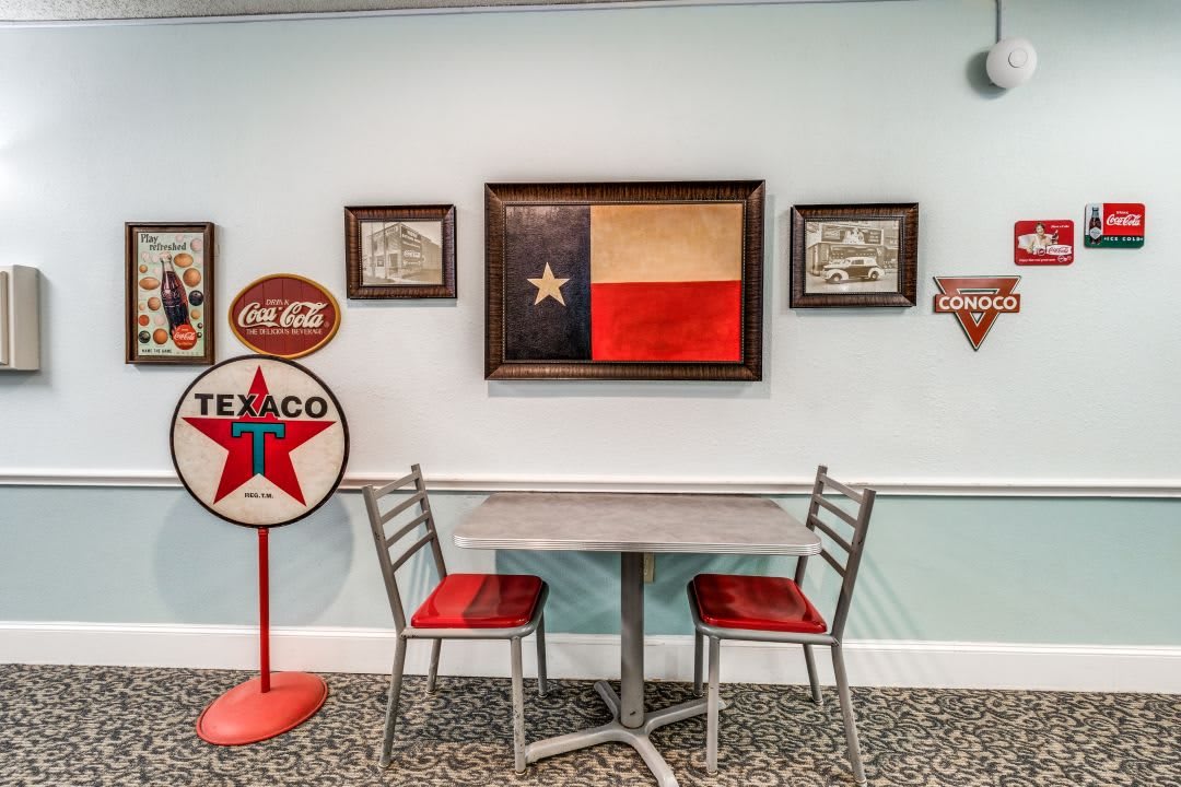 A retro-themed room featuring Texas memorabilia, including the state flag and vintage Texaco and Coca-Cola signs, with a small table and metal chairs.