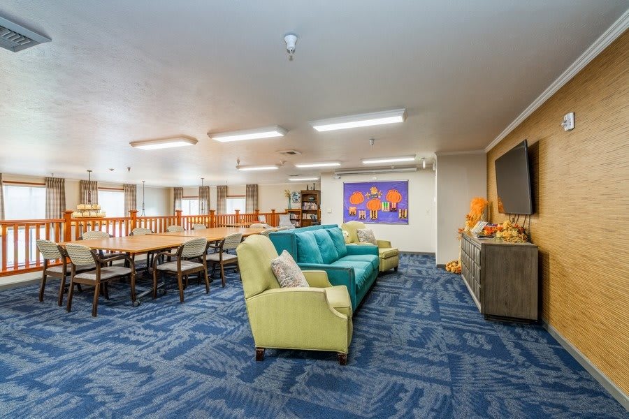 A spacious living room with colorful sofas, a long dining table, and vibrant artwork on the wall.