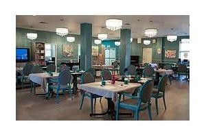 A well-decorated dining area with elegantly set tables and stylish chairs, illuminated by chandeliers.