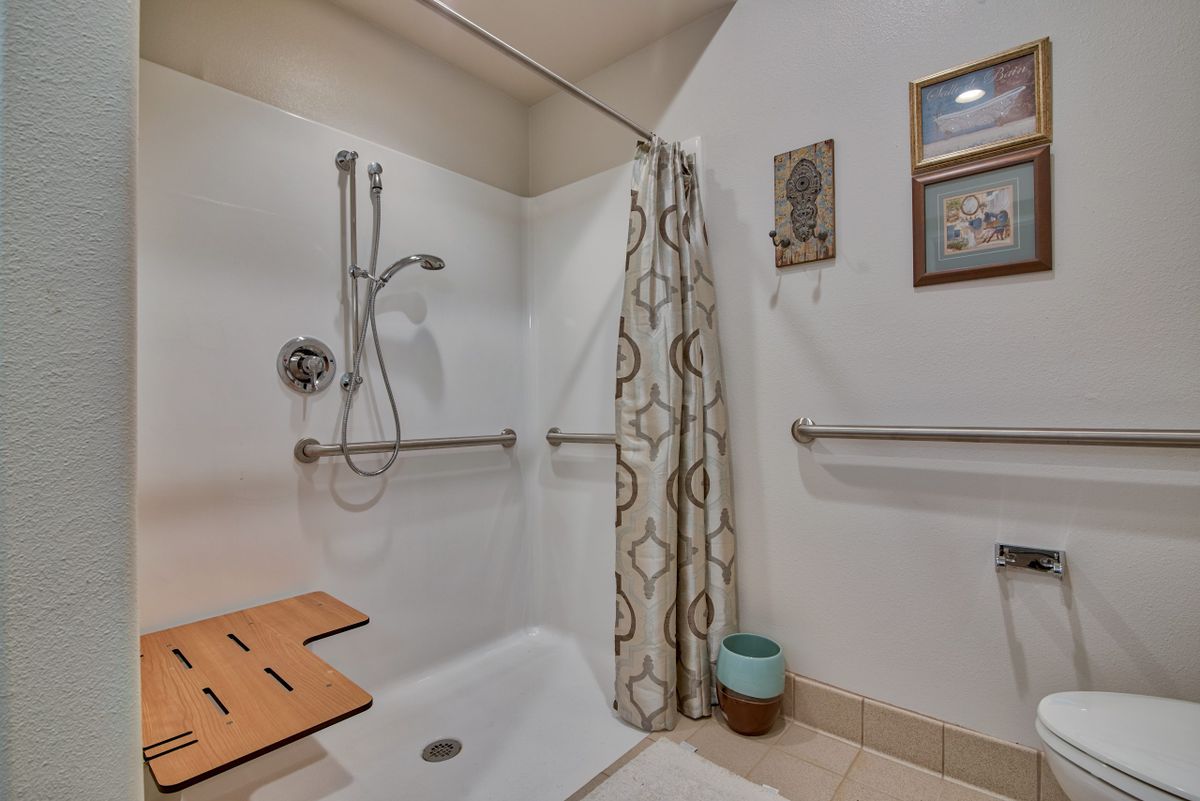An accessible bathroom with a shower featuring grab bars, a bench seat, and a decorative curtain.