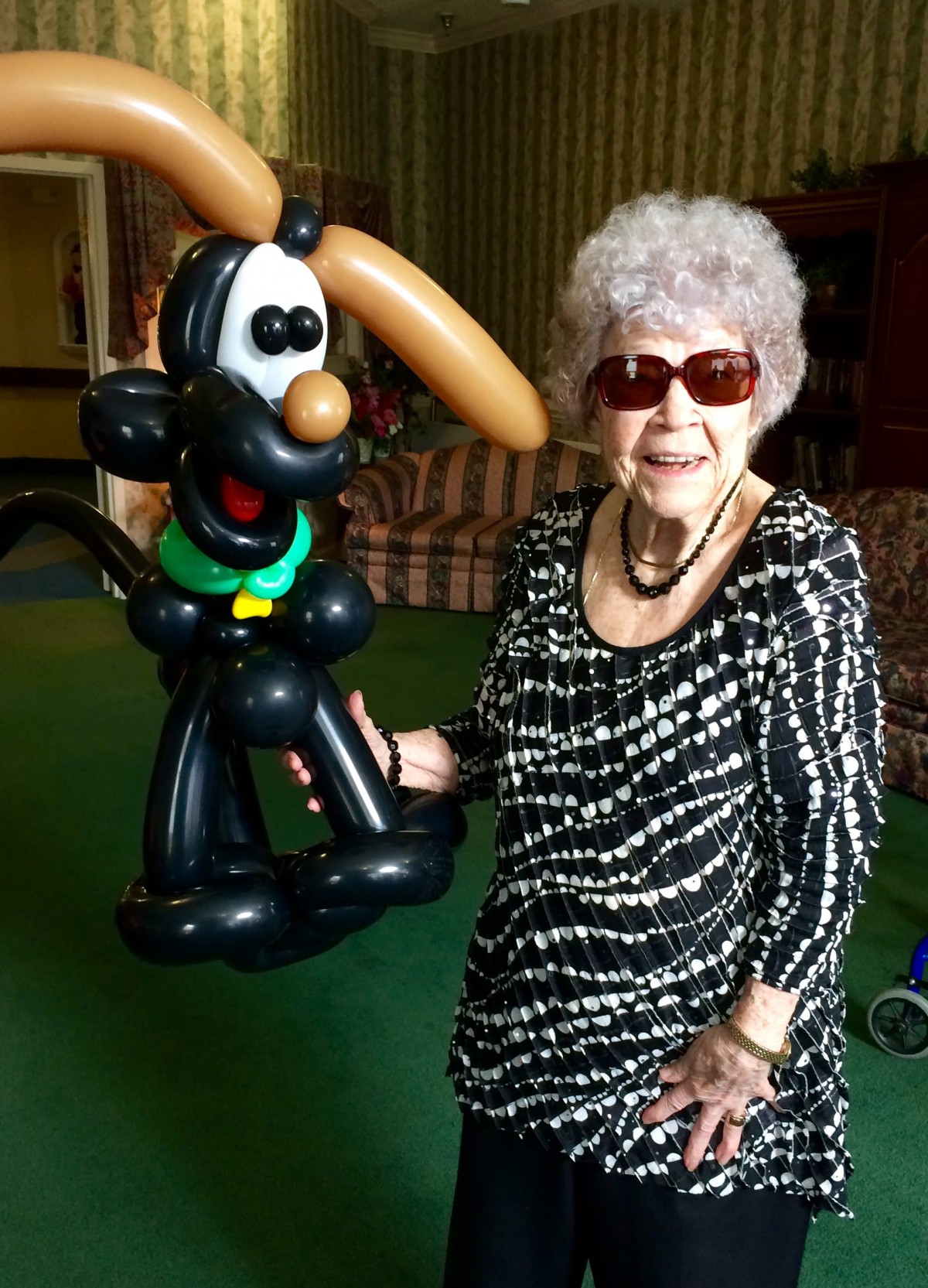 An elderly woman wearing sunglasses holding a balloon sculpture indoors.