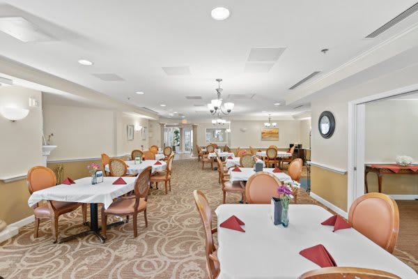 A well-lit dining room with elegantly set tables, featuring red napkins and comfortable chairs.